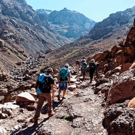 Trekkers on a rocky path through a steep valley in the High Atlas