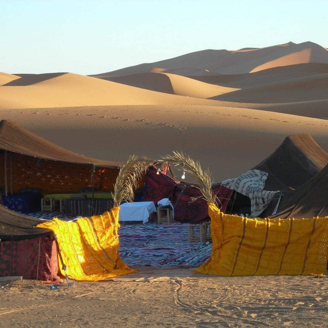 Entrance to a desert camp with carpets and tents in the dunes