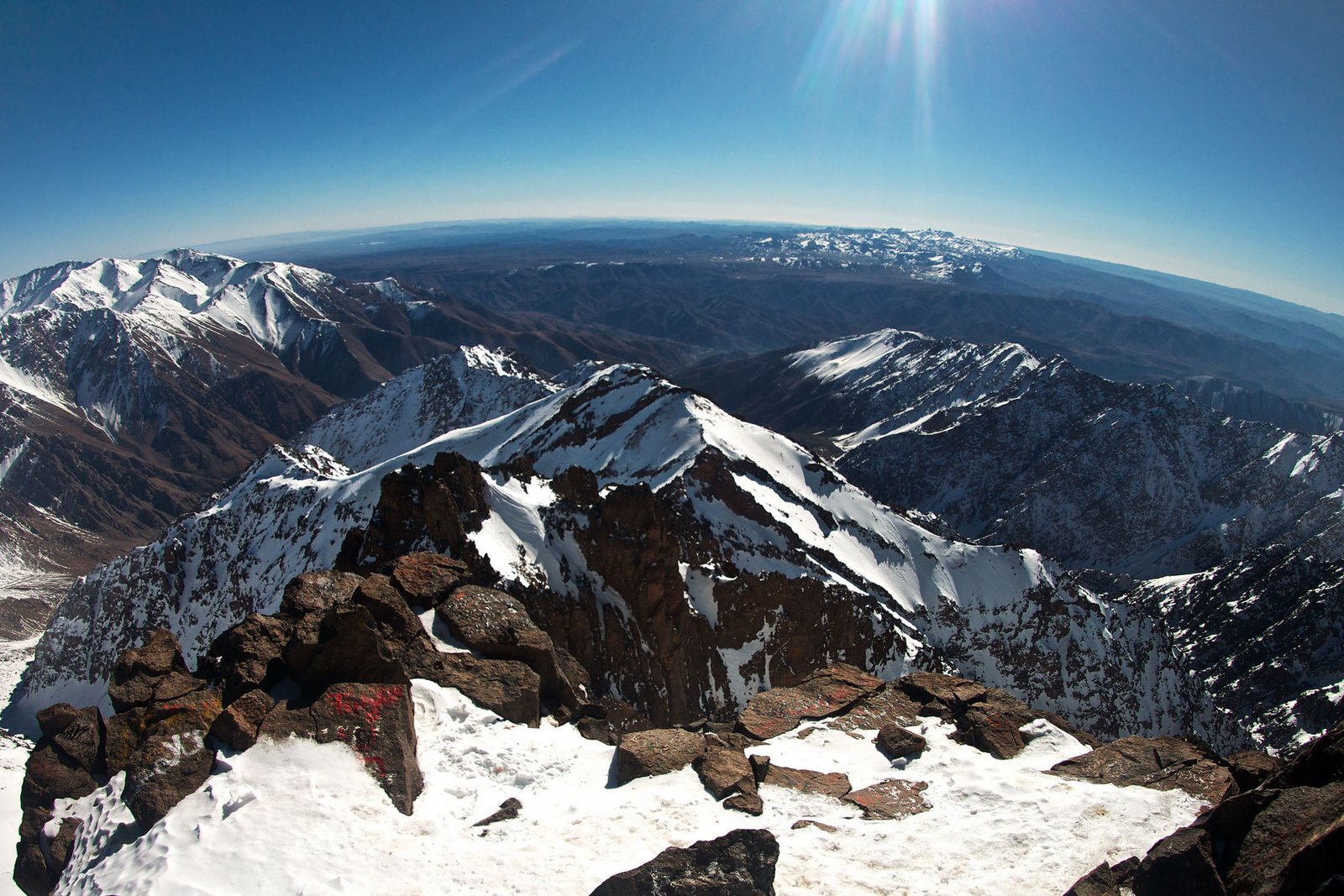 Snowy High Atlas ridges seen from a rocky summit, with the plains beyond
