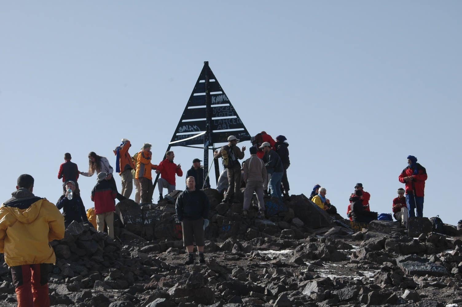 Large group of trekkers celebrating at the Toubkal summit marker