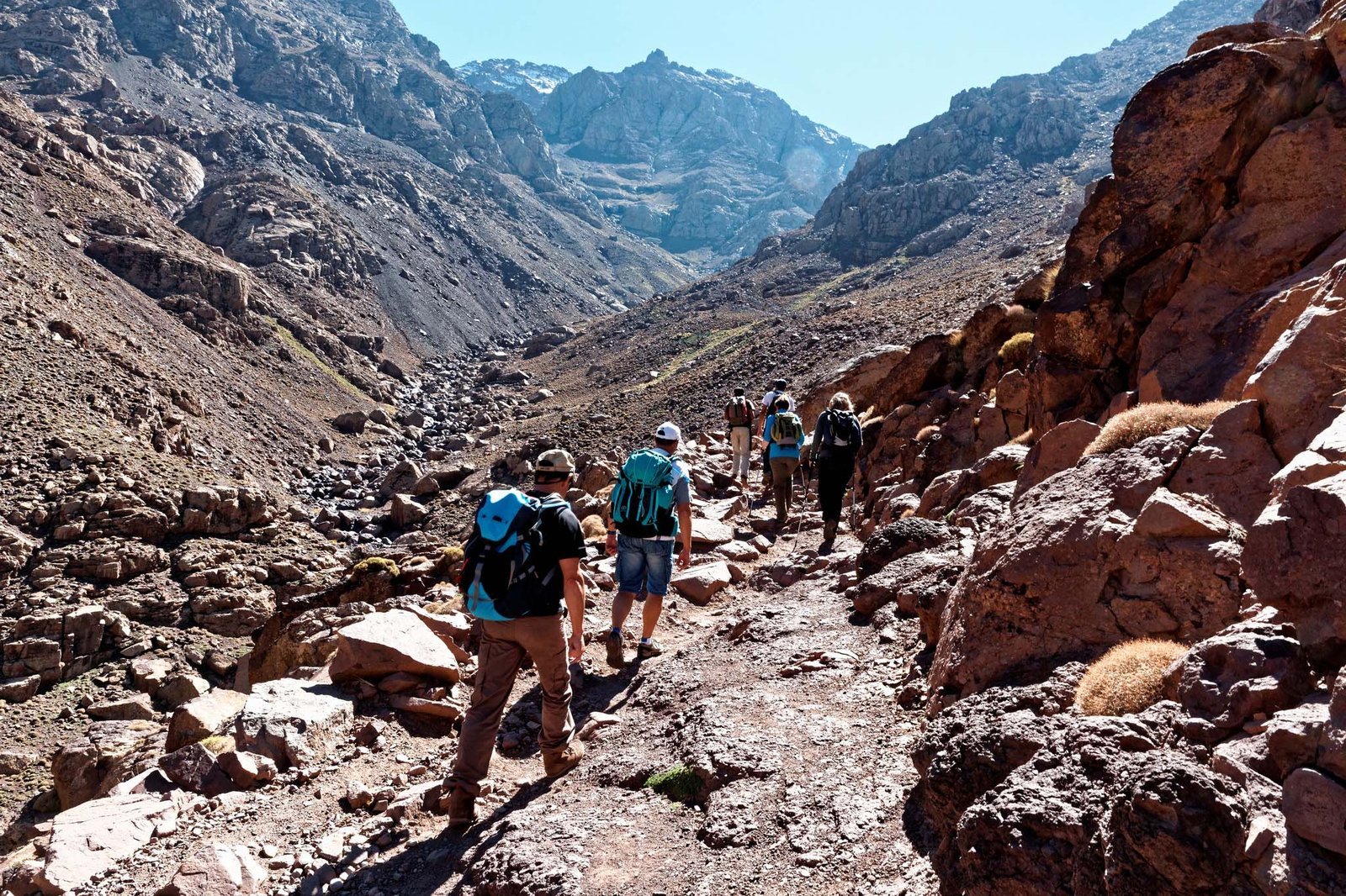 Trekkers on a rocky path through a steep red-rock valley in the High Atlas