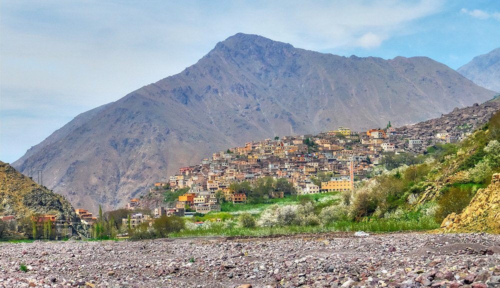 Berber village on a hillside below a High Atlas peak, above a wide stony riverbed