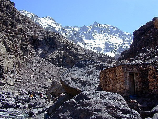 Stone hut on the rocky path towards Sidi Chamharouch, below snowy peaks