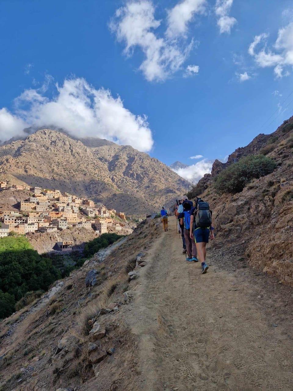 Hikers on a dirt path leading towards a Berber village in the Atlas Mountains