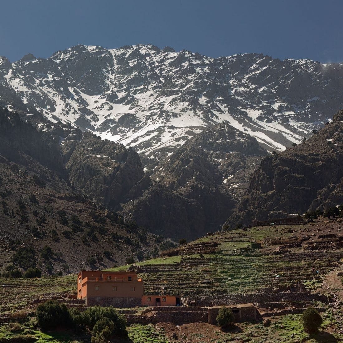 Farmhouse and terraces below a snow-streaked High Atlas ridge