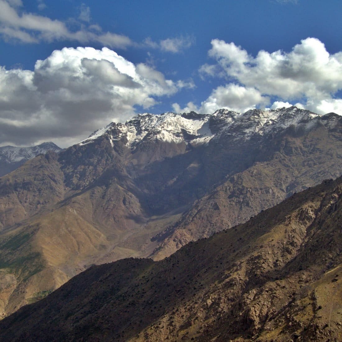 Snowy High Atlas summits under white clouds above bare brown slopes