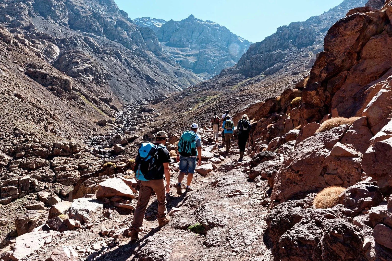 Trekkers walking a rocky trail between red rocks in a High Atlas valley