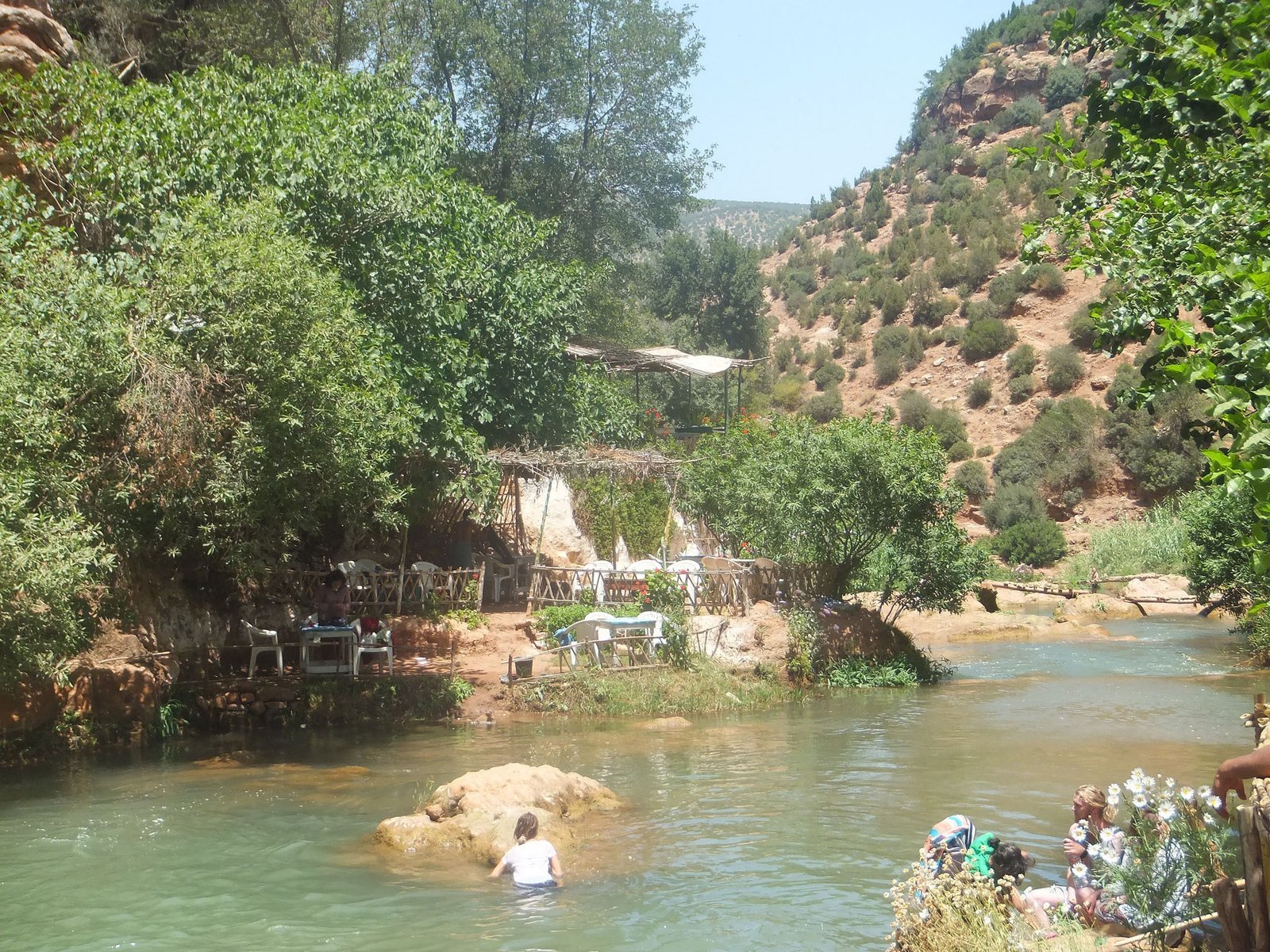 Swimmer in the river below the Ouzoud falls, with tables along the bank
