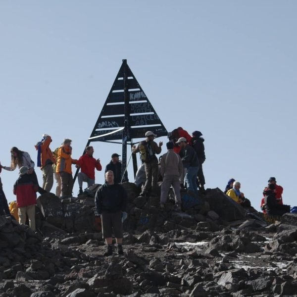 Large group of trekkers at the summit marker on top of Mount Toubkal